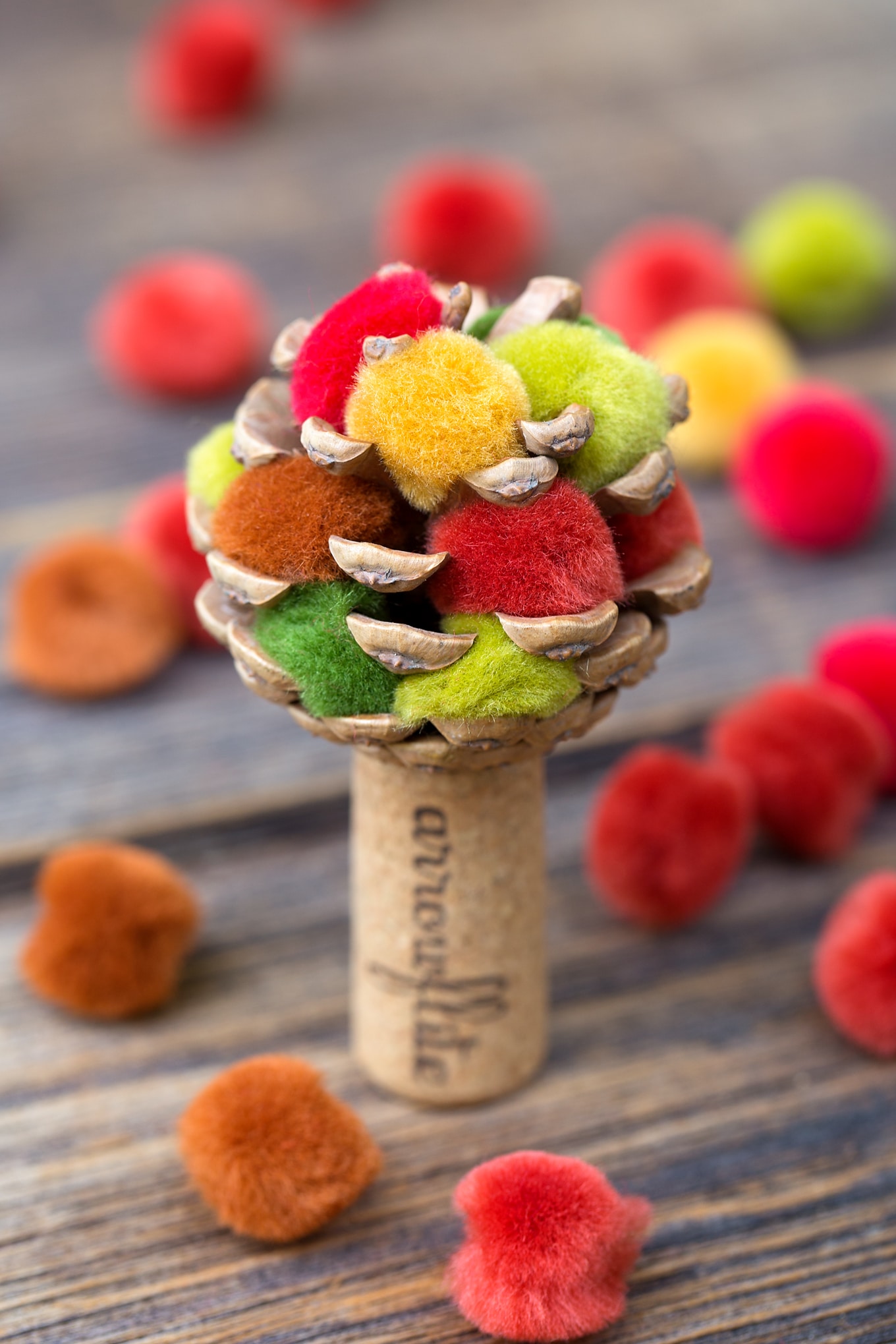 Learn how to make a colorful fall pine cone tree with pine cones, corks, and pom poms. This easy fall nature craft is perfect for kids of all ages!