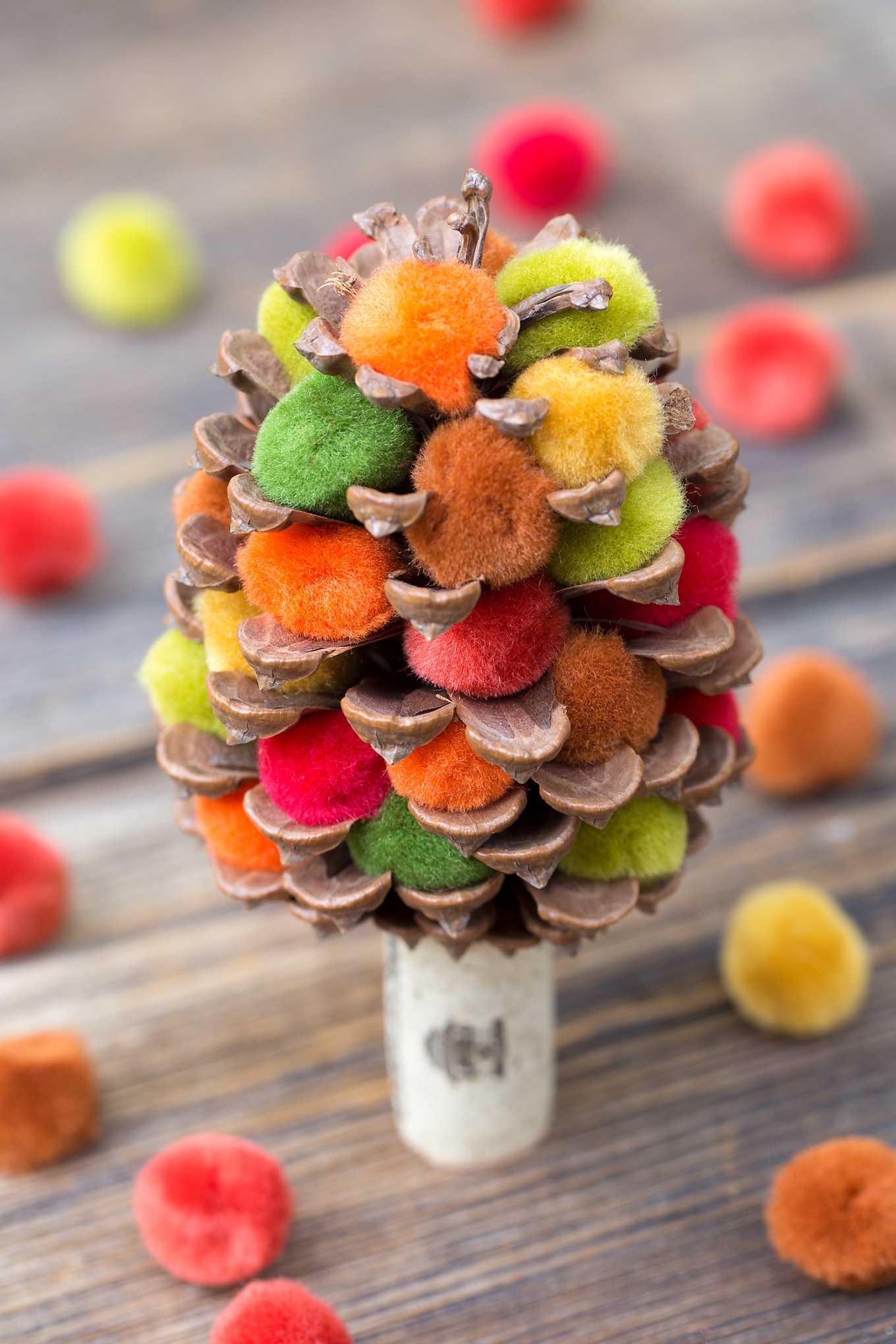 Learn how to make a colorful fall pine cone tree with pine cones, corks, and pom poms. This easy fall nature craft is perfect for kids of all ages!